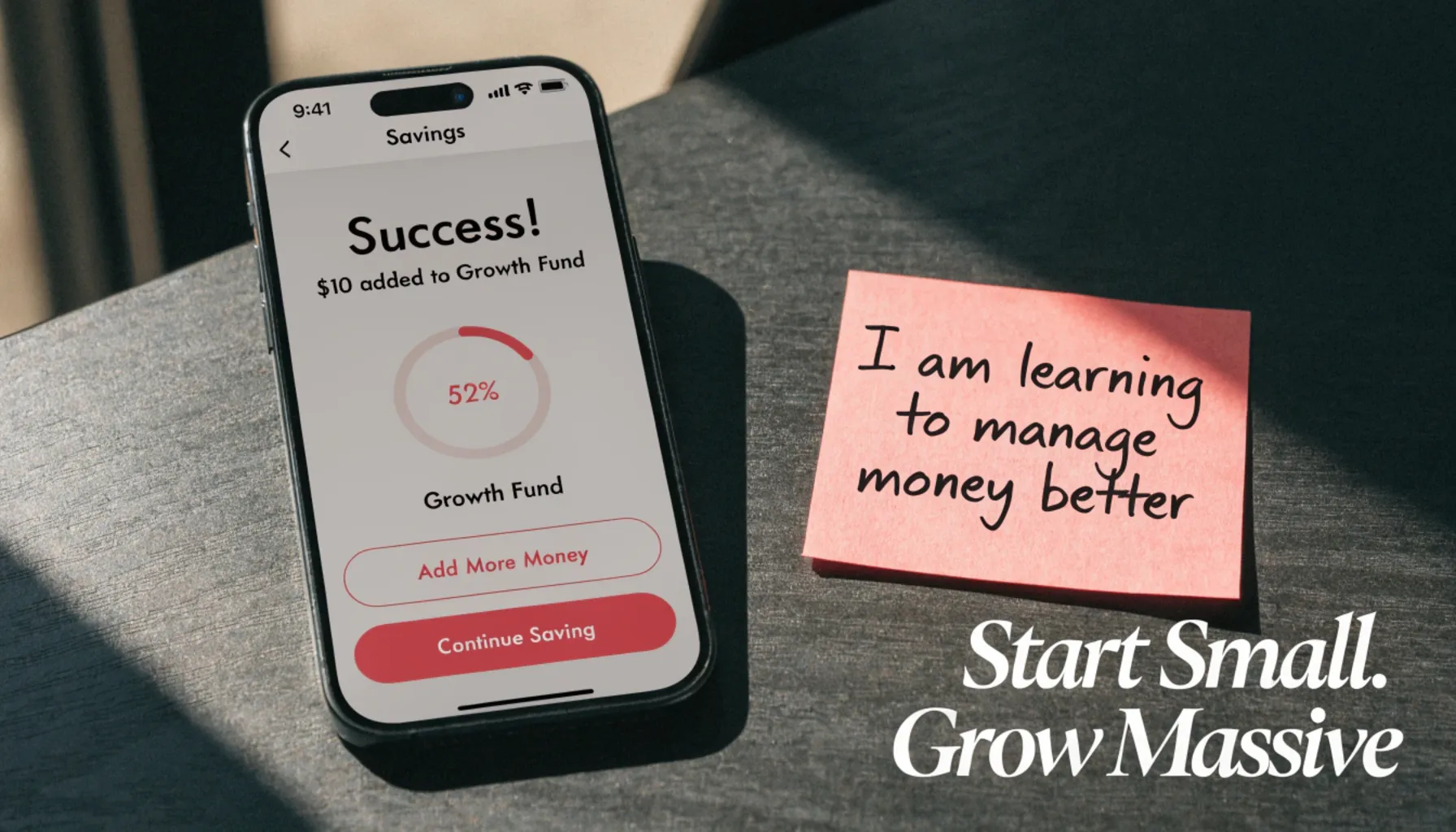 Smartphone showing a successful savings transfer and a growth mindset reframe
sticky note on a desk